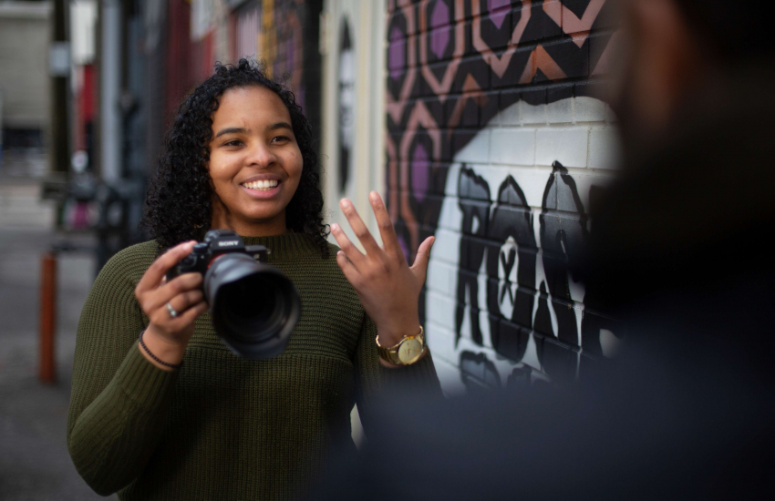 Crystal Bryan holding a camera speaking with someone at the front of the image out of focus
